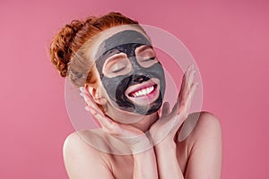 Redhaired ginger young caucasian woman with natural anti acne mask on her pretty perfect face in studio pink background
