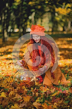 Redhaired girl in a hat collects autumn leaves in an aquarium. Concept