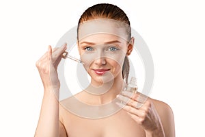 Redhaired Woman Applying Cosmetic Oil On Face Posing In Studio