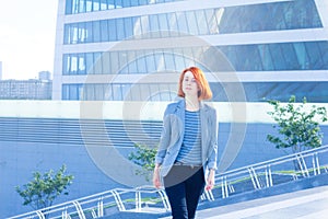 Redhead attractive business woman up the stairs on the background of a skyscraper