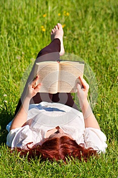 Redhead beautiful girl reading a book in nature