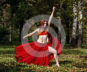 Redhead beautiful woman in red dress dancing in a autumn forest.