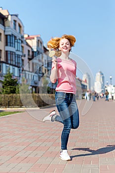 Redhead beautiful young woman jumping high in air over blue sky holding colorful lollipop. Pretty girl having fun outdoors.