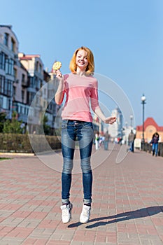 Redhead beautiful young woman jumping high in air over blue sky holding colorful lollipop. Pretty girl having fun outdoors.