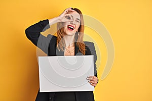 Redhead business caucasian woman holding banner over yellow isolated background with happy face smiling doing ok sign with hand on