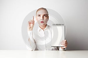 Redhead business woman posing in shirt holding empty notepad over white background.