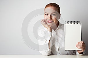 Redhead business woman posing in shirt holding empty notepad over white background.