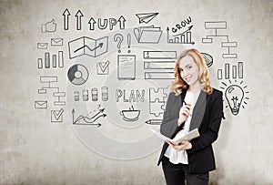 Redhead businesswoman with a notebook near a concrete wall with