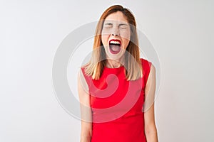Redhead businesswoman wearing elegant red dress standing over isolated white background angry and mad screaming frustrated and