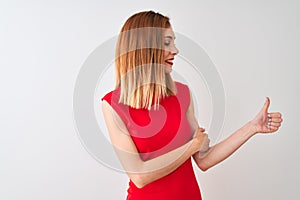 Redhead businesswoman wearing elegant red dress standing over isolated white background Looking proud, smiling doing thumbs up