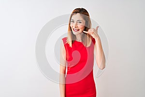 Redhead businesswoman wearing elegant red dress standing over isolated white background smiling doing phone gesture with hand and