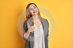 Redhead caucasian business woman over yellow isolated background doing happy thumbs up gesture with hand