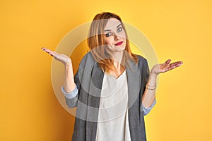 Redhead caucasian business woman over yellow isolated background looking to the side with arms crossed convinced and confident