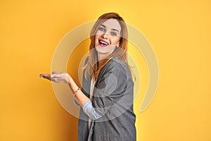 Redhead caucasian business woman over yellow isolated background pointing aside with hands open palms showing copy space,