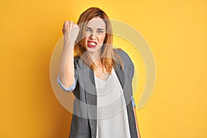 Redhead caucasian business woman over yellow isolated background Shouting frustrated with rage, hands trying to strangle, yelling photo