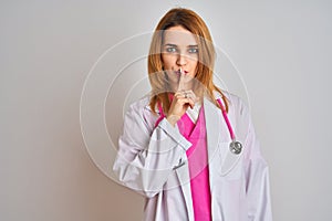 Redhead caucasian doctor woman wearing pink stethoscope over isolated background asking to be quiet with finger on lips