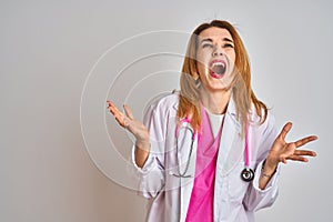 Redhead caucasian doctor woman wearing pink stethoscope over isolated background crazy and mad shouting and yelling with