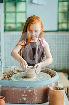 Redhead Child sculpts from clay pot. workshop on modeling on potter`s wheel.