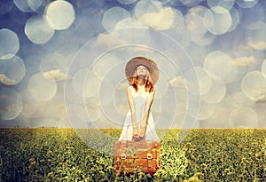 Redhead enchantress with suitcase at spring rapeseed field.