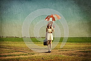 Redhead enchantress with umbrella and suitcase at spring country