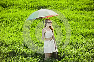 Redhead enchantress with umbrella and suitcase at spring country