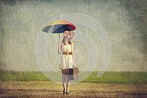 Redhead enchantress with umbrella and suitcase at spring country