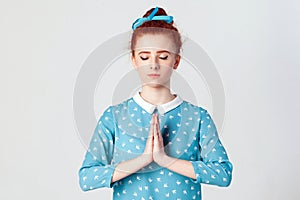 Redhead female, holding hands in namaste or prayer, keeping eyes closed while practising yoga and meditating at home alone