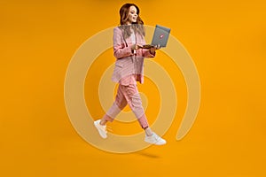 Redhead female run jump typing laptop wearing elegant pink suit  on yellow background