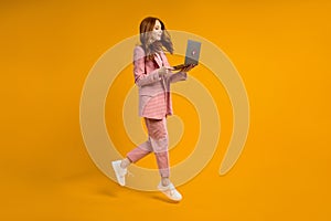 Redhead female run jump typing laptop wearing elegant pink suit  on yellow background