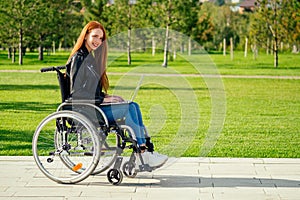 Redhead ginger freelancer woman sitting in wheelchair and working by laptop in summer park