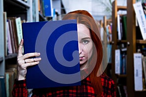 Redhead girl with blue book in a library