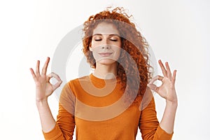 Redhead girl calm down, soothing stress with yoga. Relieved happy ginger woman peacefully meditating, making zen mudra photo