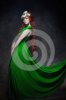 Redhead girl fabulous look, green long dress, bright makeup and big eyelashes. Mysterious fairy woman with red hair. Big eyes and