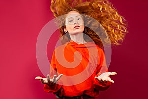 Redhead girl with flutter curly hair. Looks at the camera on a red background.