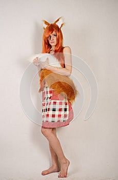 Redhead girl with fur ears and tail posing in kitchen apron on white background in Studio