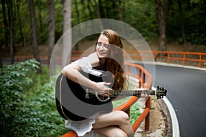 Redhead Girl with a guitar singing in a road trip