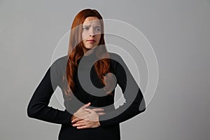 The redhead girl has awful stomachache at gray background her home