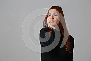 The redhead girl has horrible toothache at gray background her home