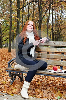 Redhead girl with headphones listen music on player in city park, fall season