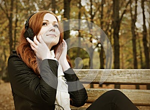 Redhead girl with headphones listen music on player in city park, fall season