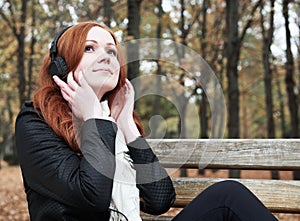 Redhead girl with headphones listen music on player in city park, fall season