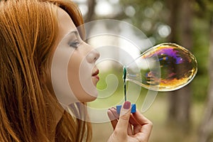 Redhead girl inflate soap bubble