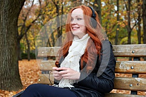 Redhead girl listen music in city park, fall season