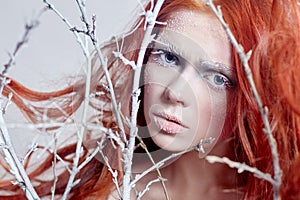 Redhead girl with long hair, a face covered with snow with frost. White eyebrows and eyelashes in frost, a tree branch covered