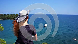 Redhead girl looks from a hill on the Mediterranean Sea with a yacht in Phaselis. City of ancient Lycia. Turkey.