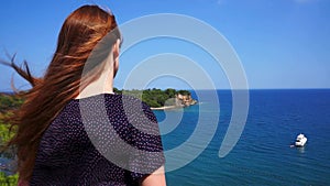 Redhead girl looks from a hill on the Mediterranean Sea with a yacht in Phaselis. City of ancient Lycia. Turkey.