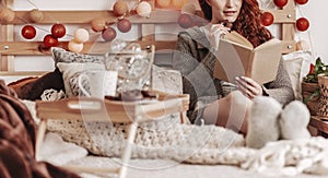 Redhead girl reading book in bed and eating cookie in cozy bedroom interior