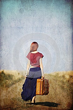 Redhead girl with suitcase at countryside road