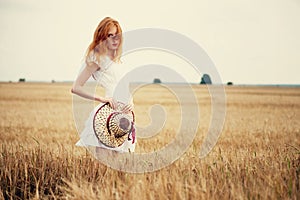 Redhead girl at summer wheat field holding hat