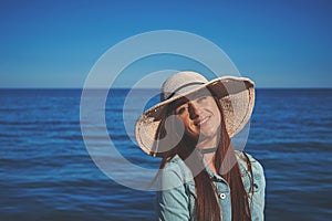 Redhead girl wearing black dress and jeans jacket. Straw hat. Woman standing on sand. Retro toned image.